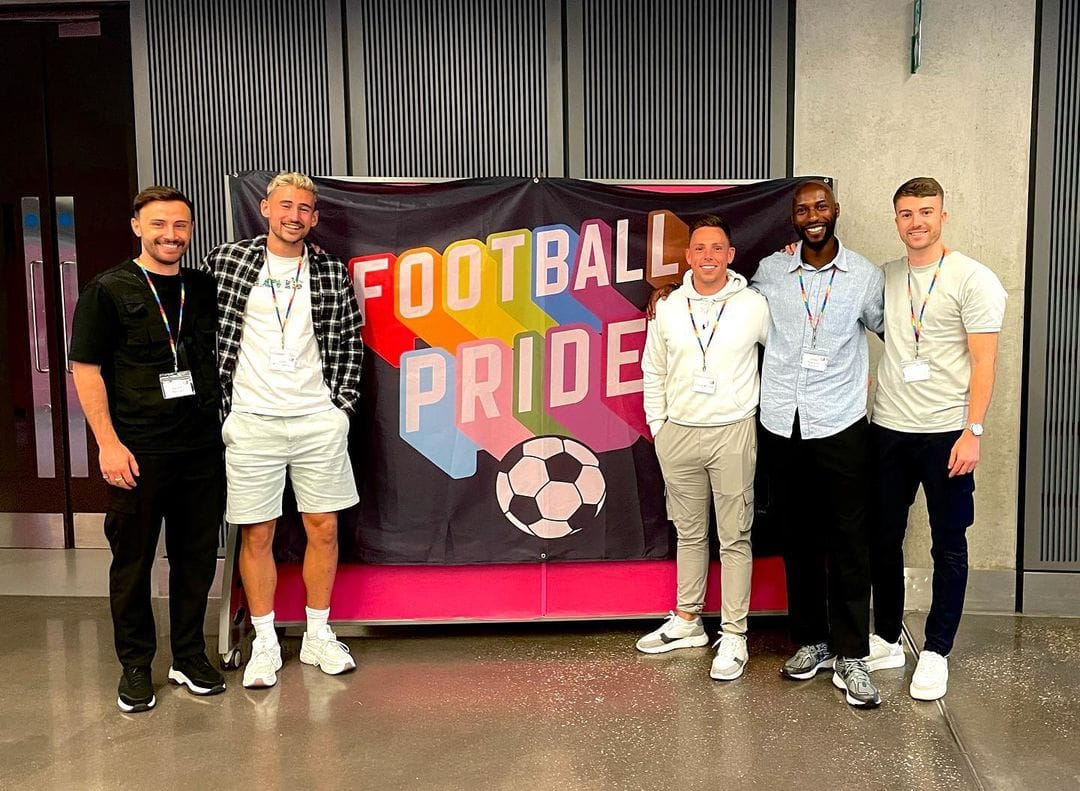 Five men stand smiling in front of a banner that reads "Football Pride".